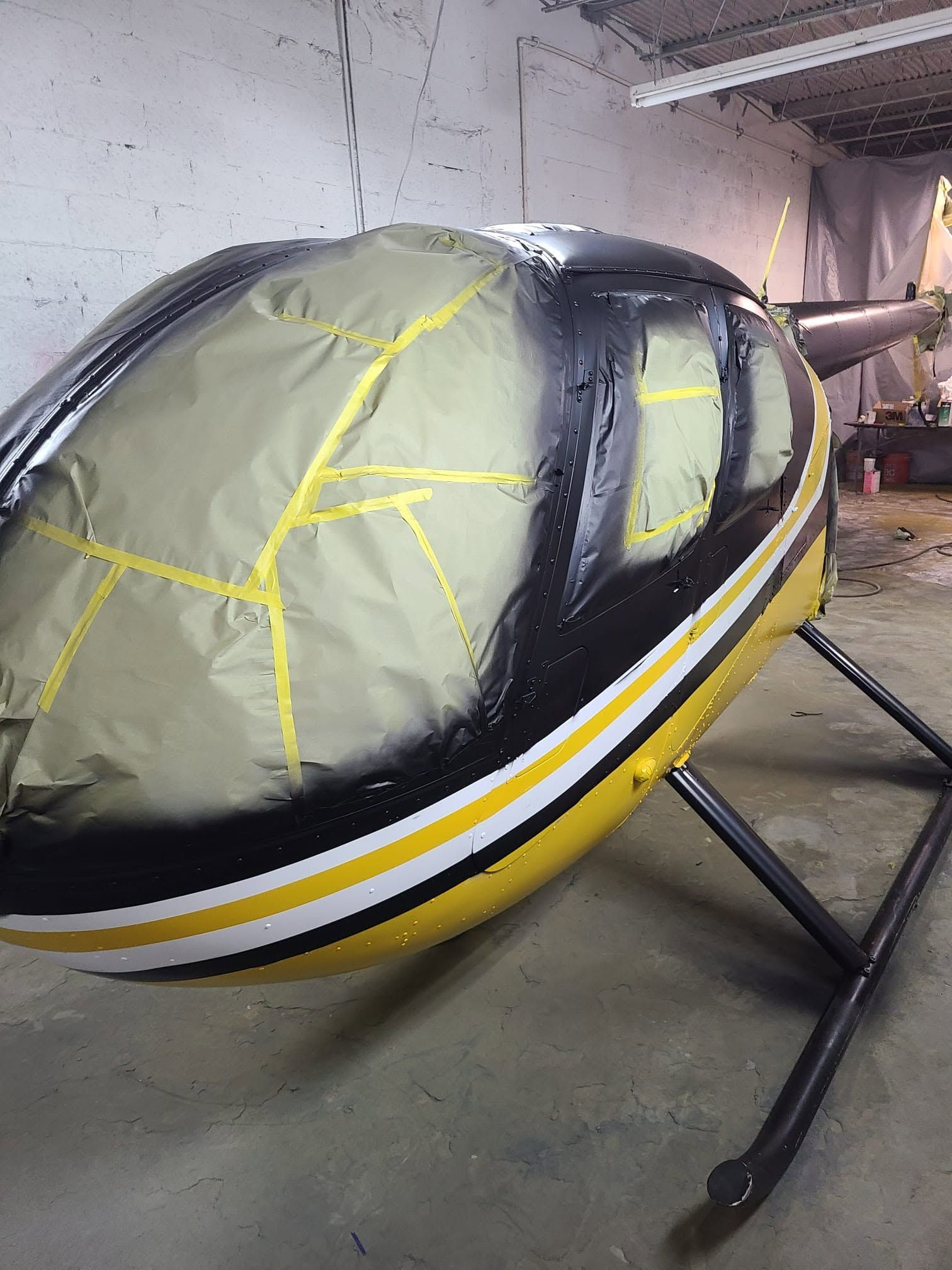 Helicopter freshly painted in black, yellow and white, with windows masked off with paper and tape during the paint process.