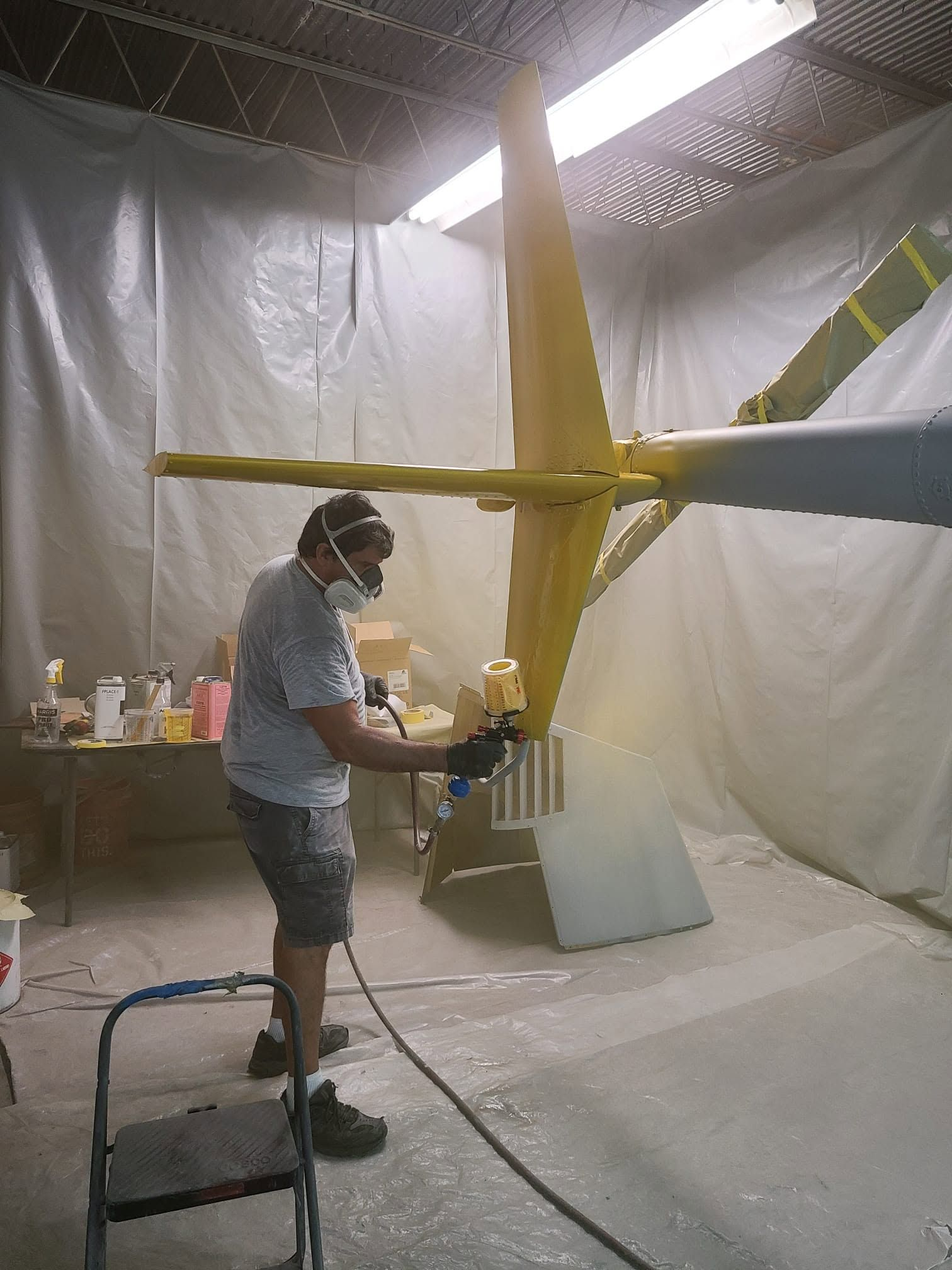 Technician spray-painting a helicopter tail section yellow inside a protected paint booth.