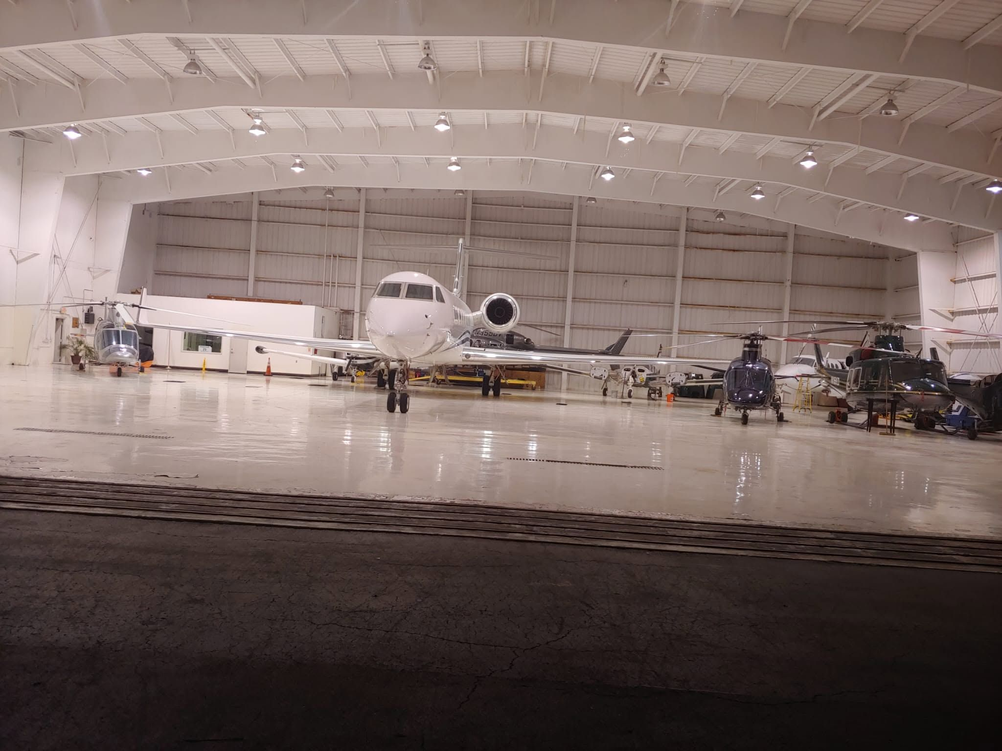 Private aviation hangar housing a business jet, helicopters and turboprop aircraft in a clean, well-lit facility.