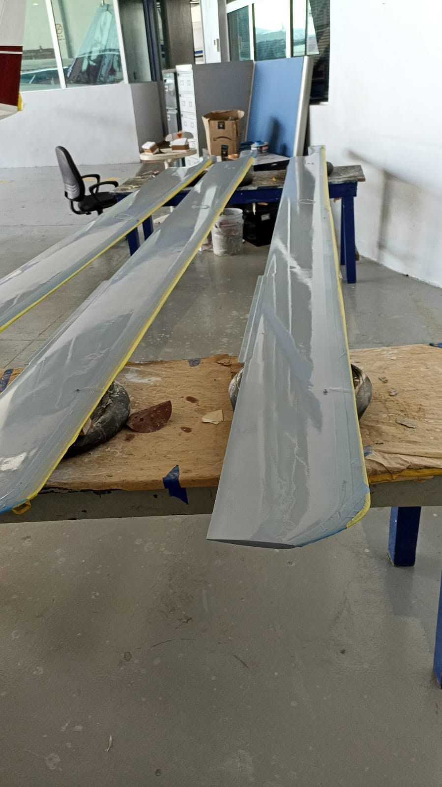 Helicopter rotor blades with a freshly applied gray finish, resting on workbenches in the hangar paint shop.