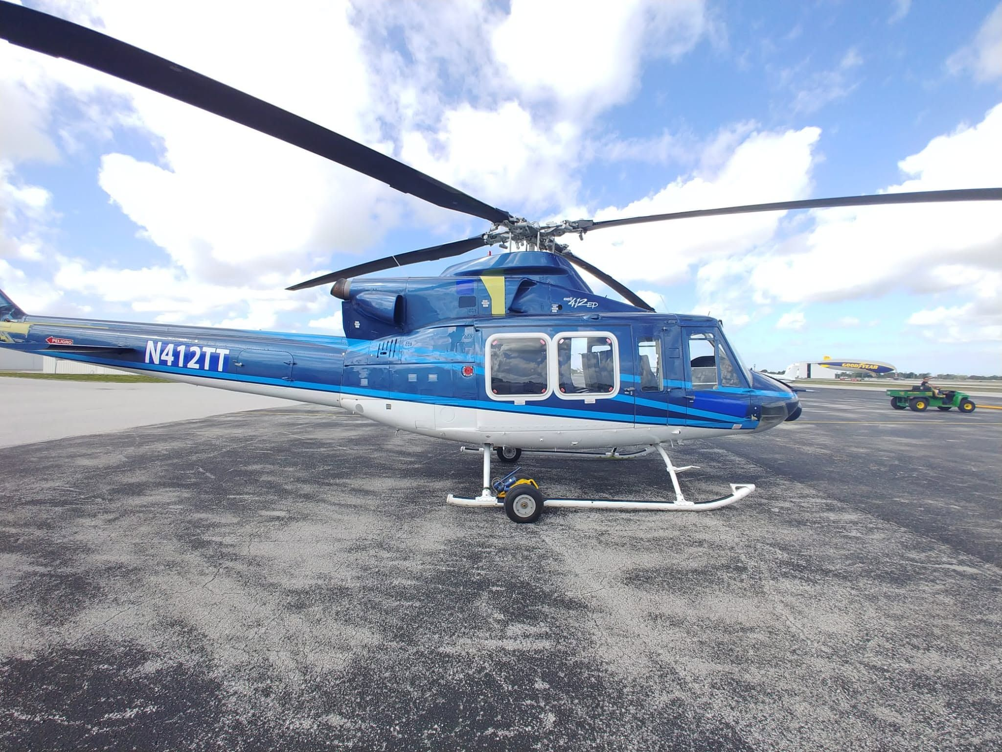 Bell 412EP helicopter in blue and white livery, parked on the ramp with ground-handling wheels attached.