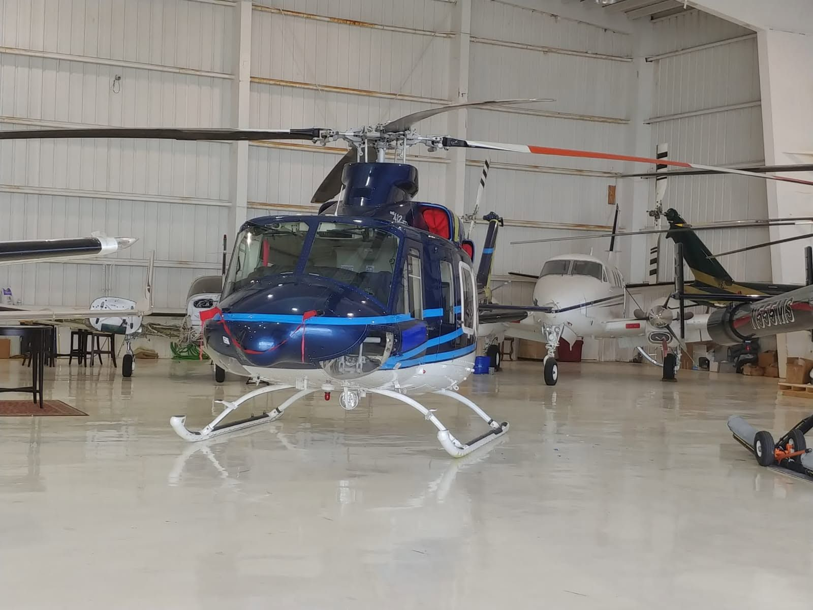 Bell 412EP helicopter in blue and white livery, parked inside the hangar alongside a turboprop and other aircraft.