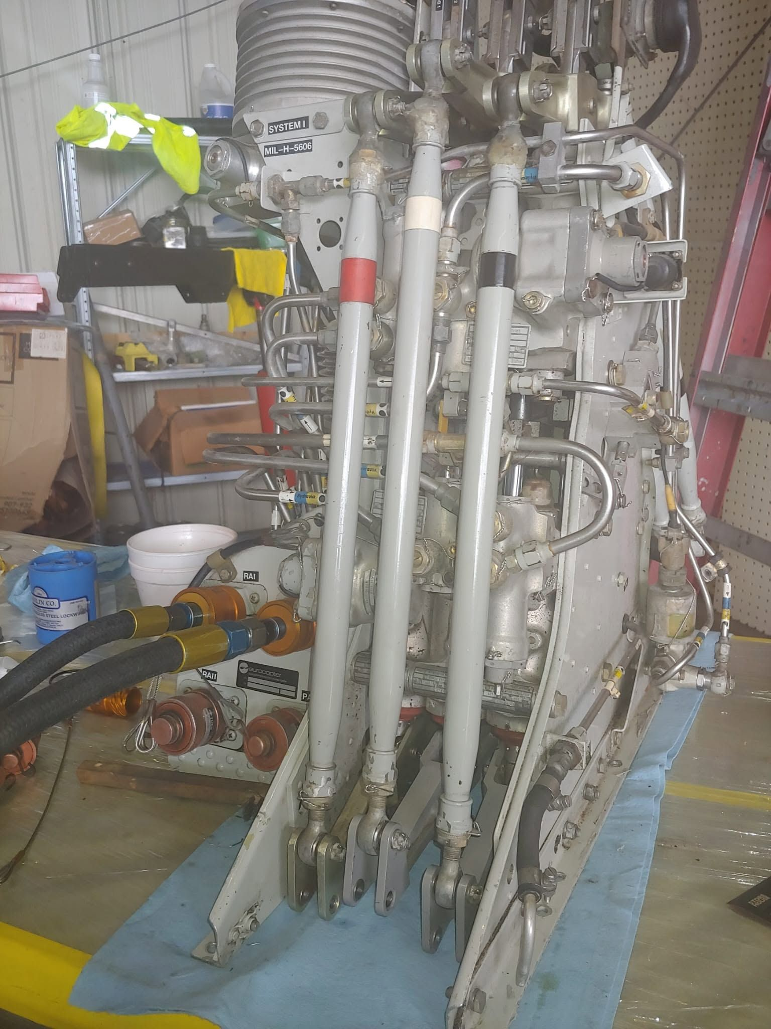 Eurocopter helicopter hydraulic system and flight control servo assembly on the workbench, connected to test lines during maintenance.