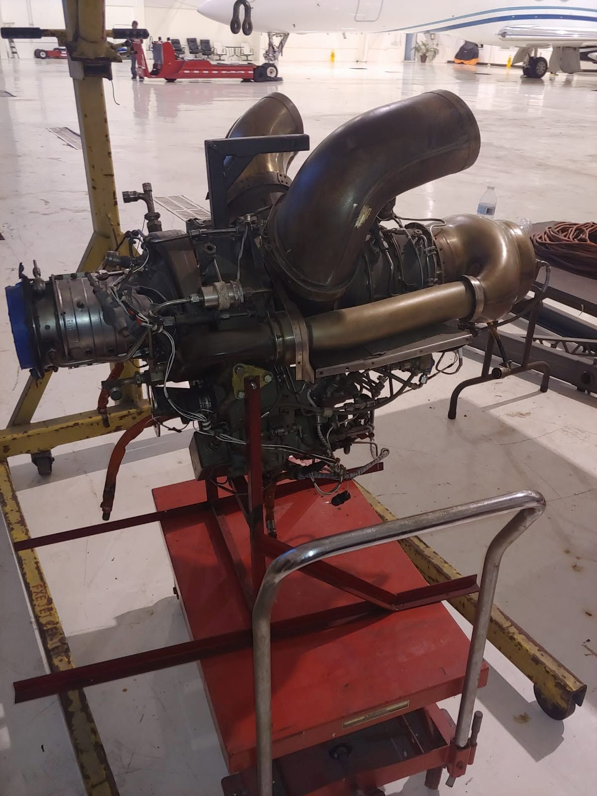 Helicopter turboshaft engine removed for maintenance, mounted on a lift cart inside the hangar.
